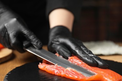 Photo of Chef in gloves cutting salmon for sushi at table, closeup