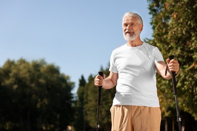 Senior man practicing Nordic walking with poles outdoors on sunny day