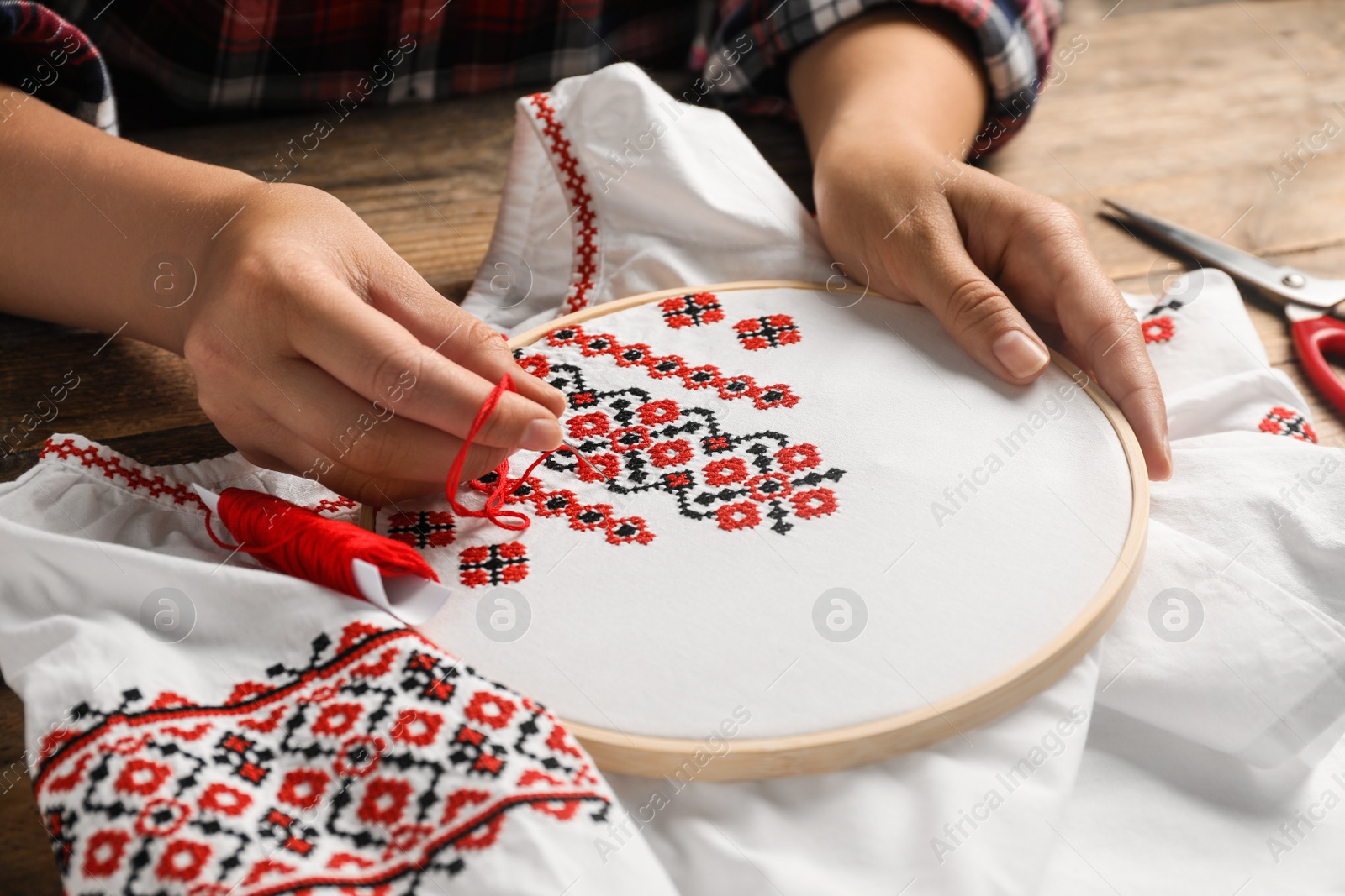 Photo of Woman embroidering white shirt with colorful threads at wooden table, closeup. Ukrainian national clothes