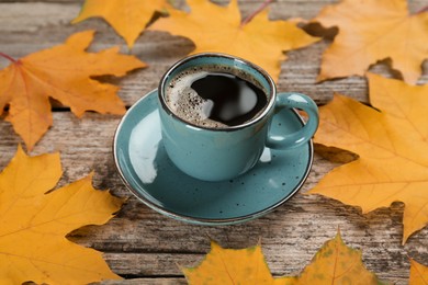 Cup of hot coffee and autumn leaves on wooden table