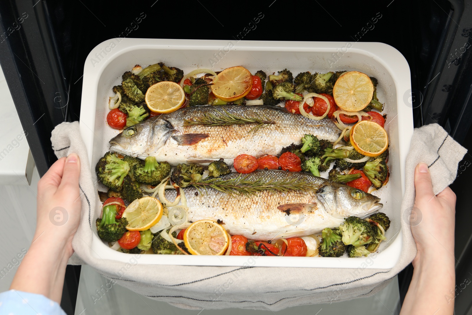 Photo of Woman taking baking dish with delicious fish and vegetables from oven, top view