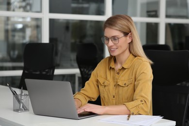 Photo of Woman working on laptop at white desk in office