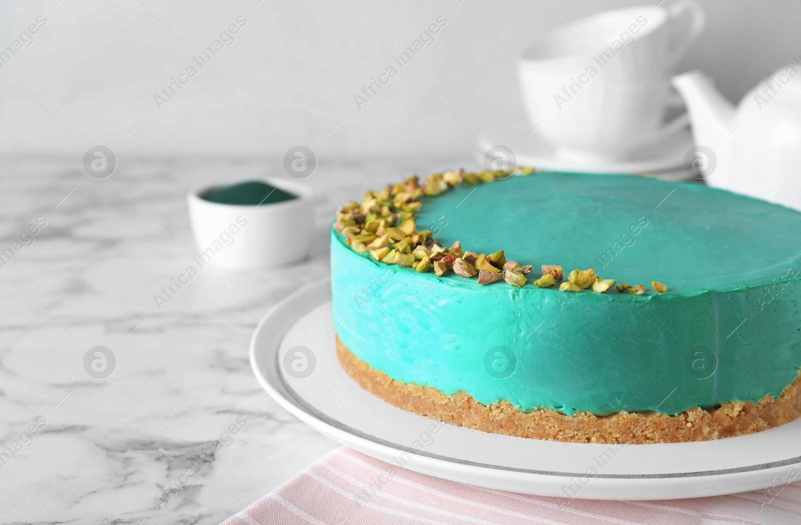 Photo of Delicious homemade spirulina cheesecake decorated with pistachios on marble table against light background