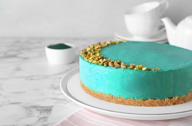 Delicious homemade spirulina cheesecake decorated with pistachios on marble table against light background