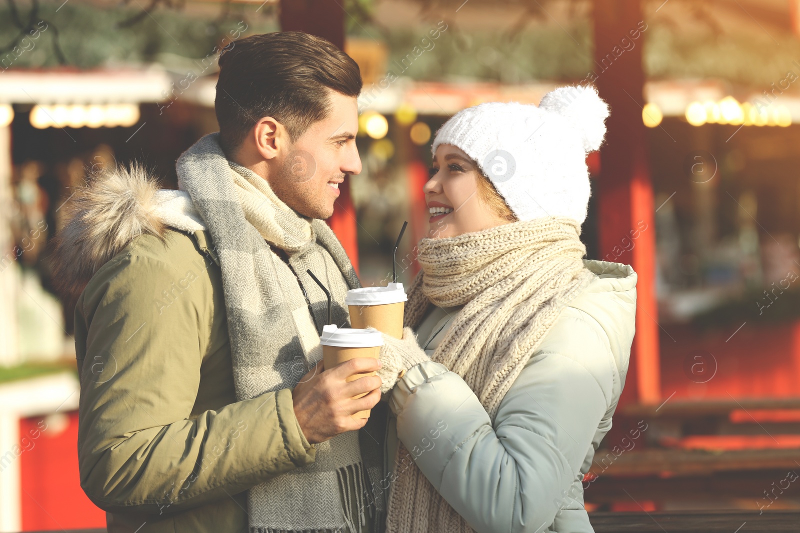 Photo of Happy couple in warm clothes with drinks at winter fair. Christmas season