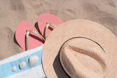 Photo of Straw hat, beach towel, seashells and flip flops on sand, flat lay