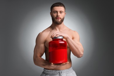 Young man with muscular body holding jar of protein powder on grey background