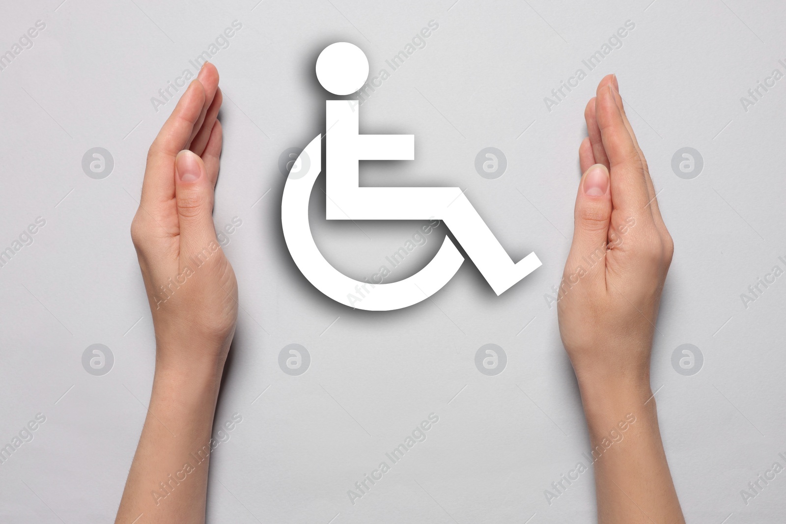 Image of Disability inclusion. Woman protecting wheelchair symbol on light background, closeup