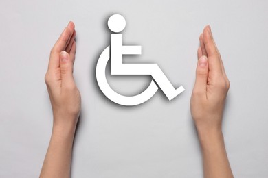 Image of Disability inclusion. Woman protecting wheelchair symbol on light background, closeup