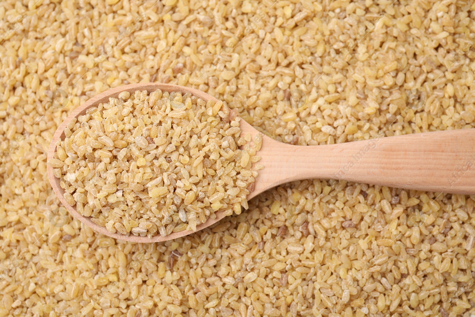 Photo of Wooden spoon and raw bulgur as background, top view