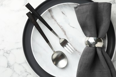 Stylish setting with cutlery, napkin and plates on white marble table, top view