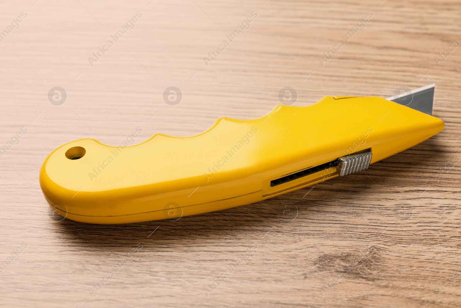 Photo of Yellow utility knife on wooden table. Construction tool