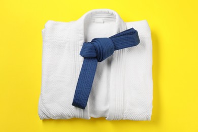 Blue karate belt and white kimono on yellow background, top view