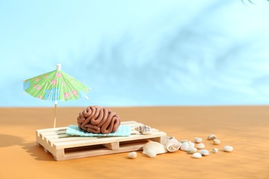 Photo of Brain made of plasticine on mini wooden sunbed under umbrella against color background, space for text