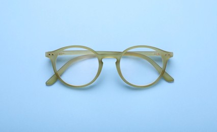 Photo of Glasses with corrective lenses on light blue background, top view