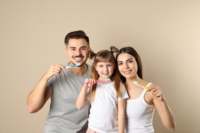 Photo of Little girl and her parents brushing teeth together on color background