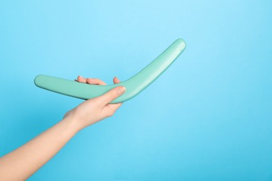 Woman holding boomerang on light blue background, closeup. Space for text