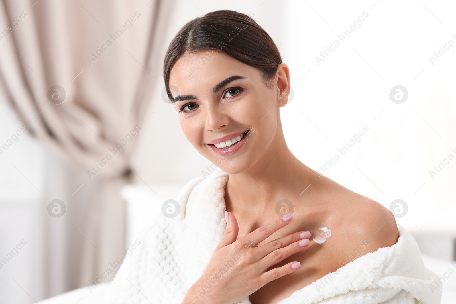 Photo of Young woman applying cream indoors. Beauty and body care