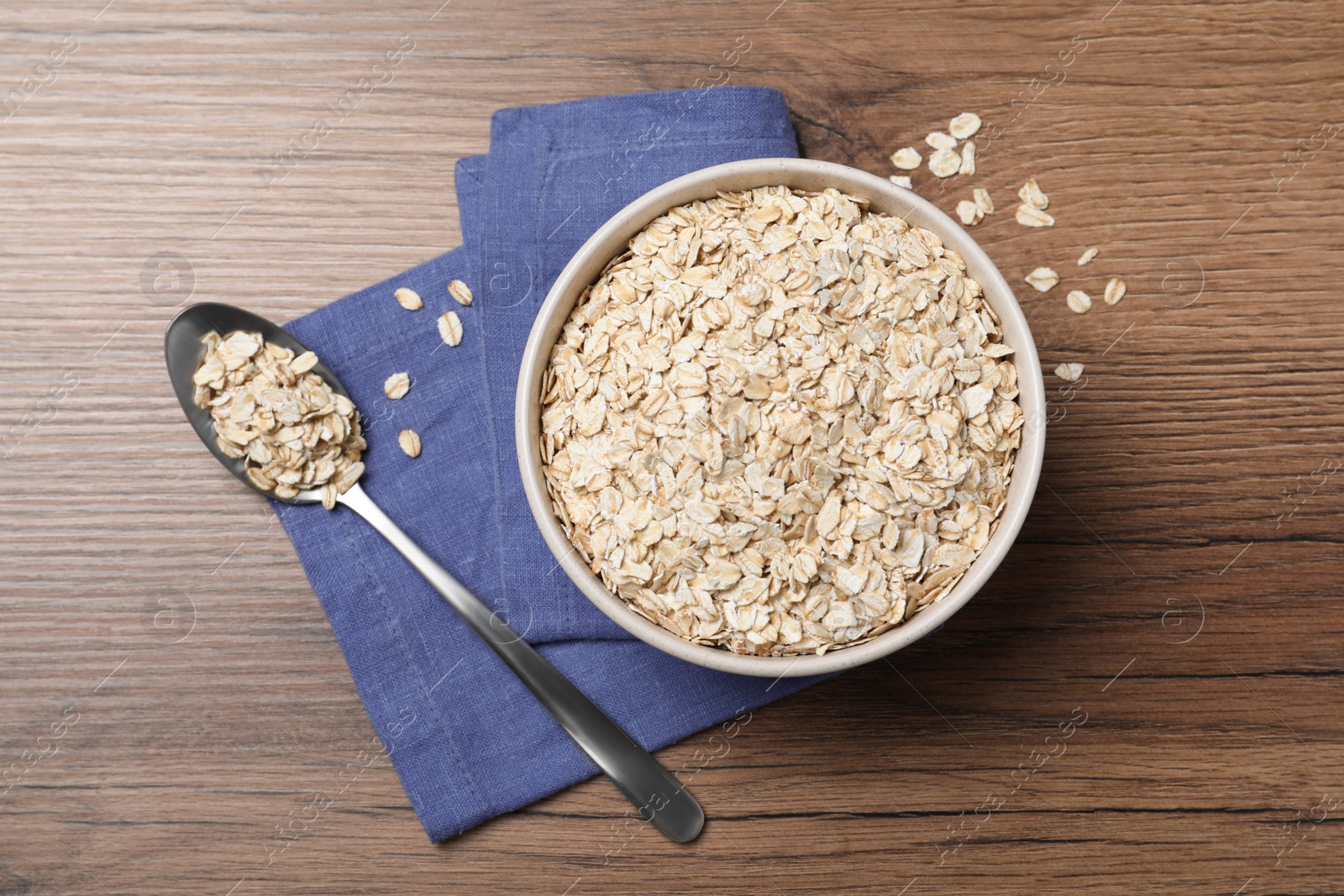 Photo of Bowl and spoon with oatmeal on wooden table, flat lay