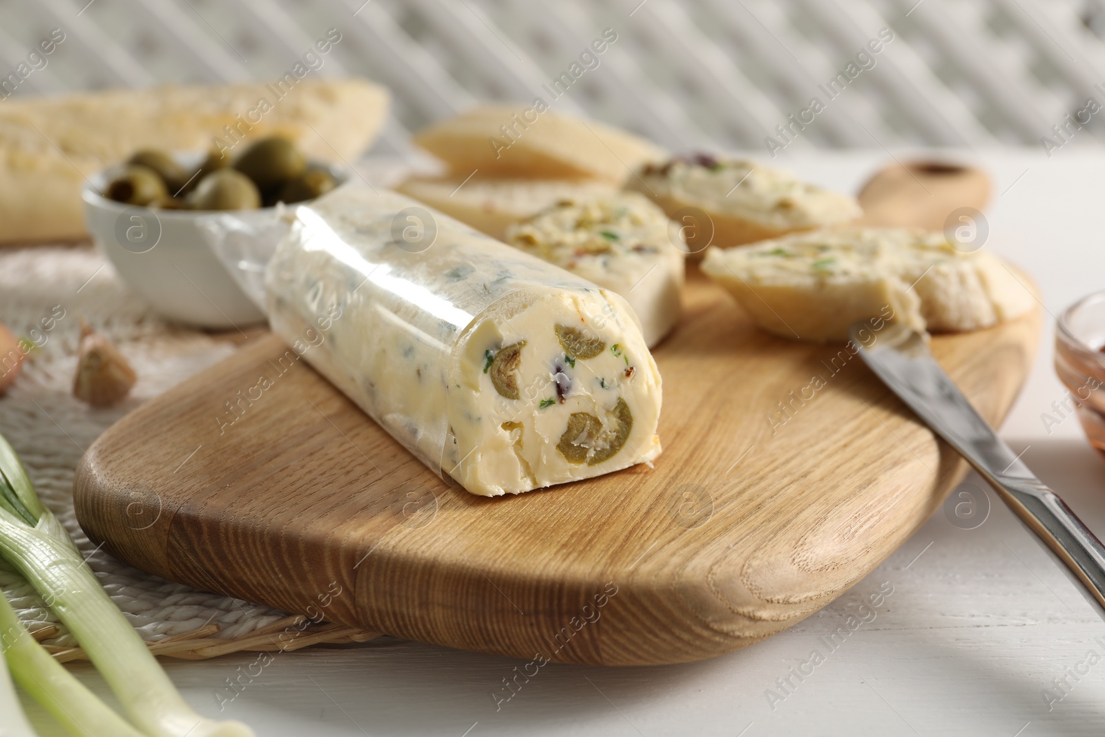 Photo of Tasty butter with olives, green onion, bread and knife on white wooden table