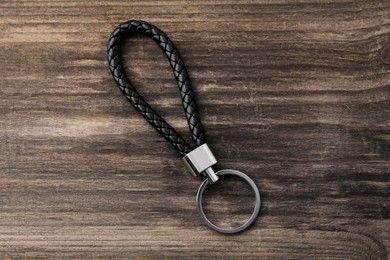 Black leather keychain on wooden background, top view