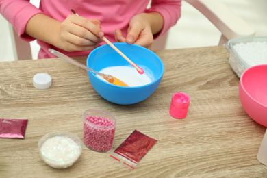 Photo of Little girl making homemade slime toy at table, closeup