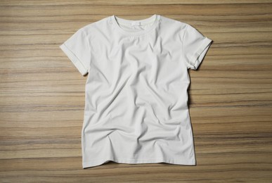 Stylish white T-shirt on wooden table, top view