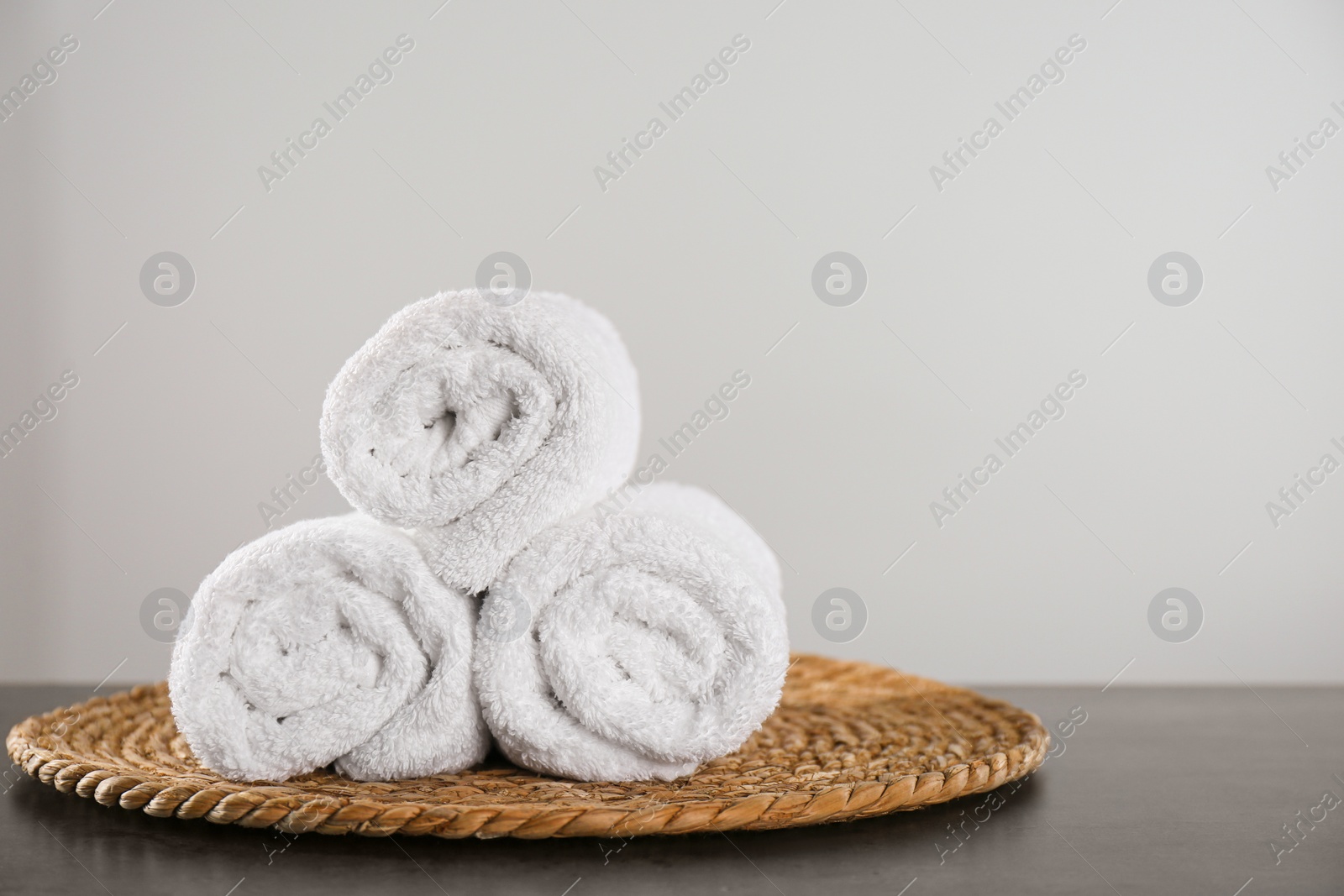 Photo of Clean rolled bath towels and wicker mat on dark grey table. Space for text