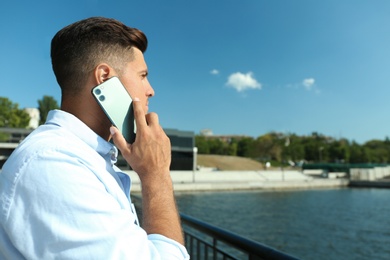 Man talking on modern mobile phone near river