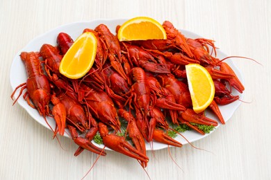Plate with delicious red boiled crayfish and orange on white wooden table, above view