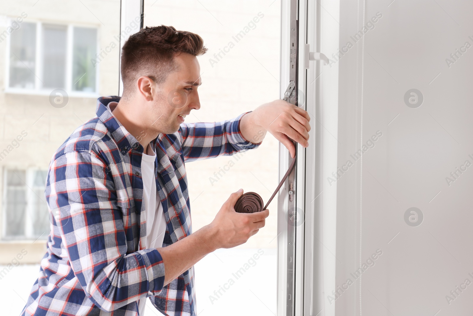 Photo of Young man putting sealing foam tape on window indoors