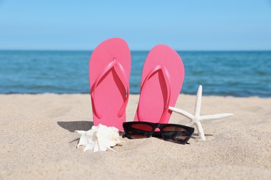 Stylish pink flip flops, sunglasses, starfish and seashell on beach sand