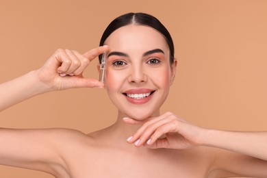 Beautiful young woman holding skincare ampoule on beige background