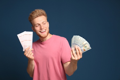 Photo of Portrait of happy young man with money and lottery tickets on blue background