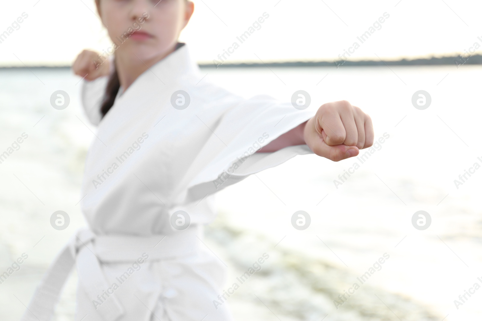 Photo of Cute little girl in kimono practicing karate near river, closeup