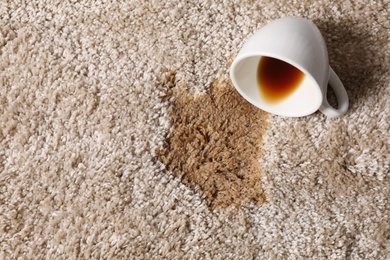 Overturned cup and spilled coffee on beige carpet, above view. Space for text