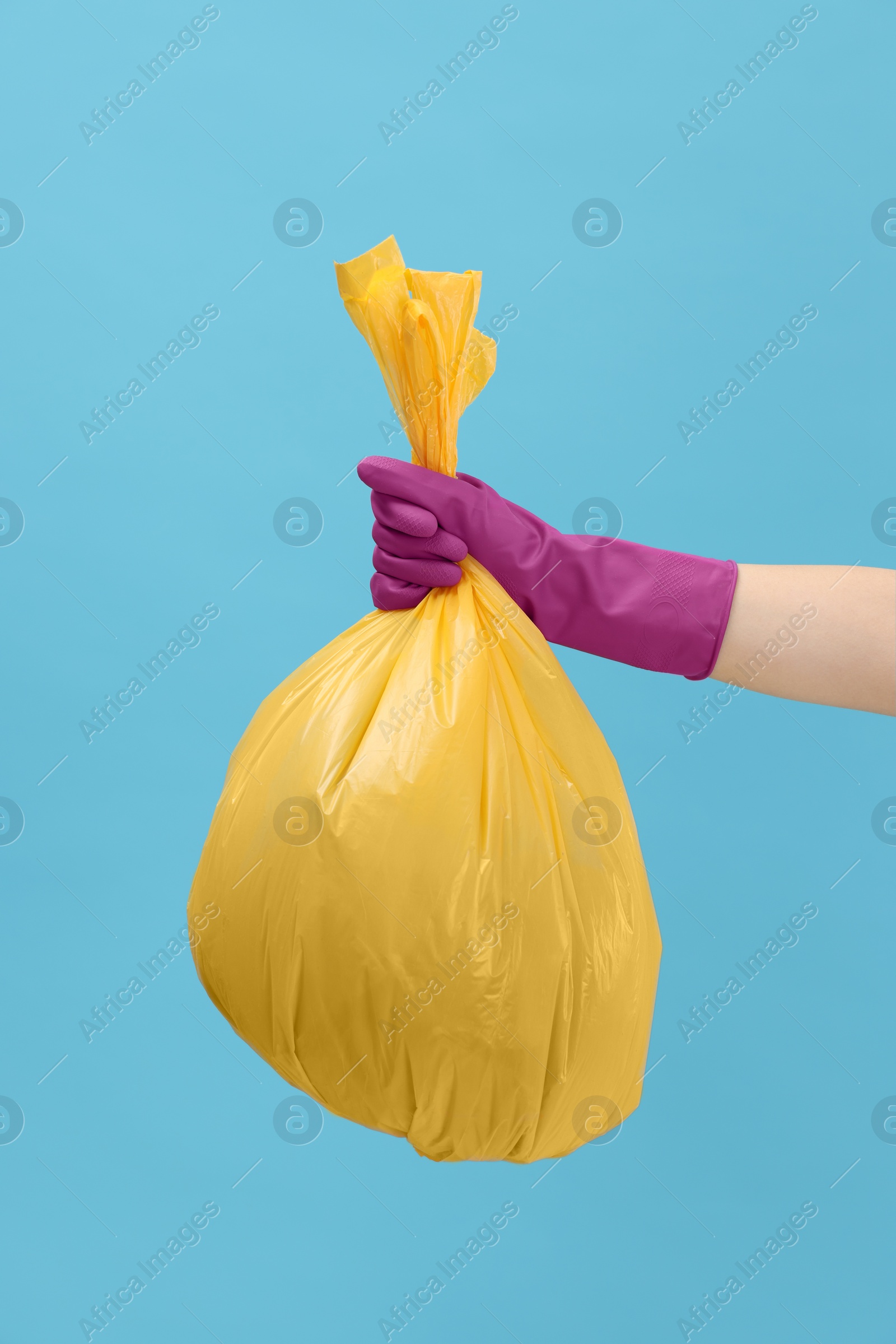 Photo of Woman holding plastic bag full of garbage on light blue background, closeup