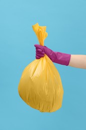 Photo of Woman holding plastic bag full of garbage on light blue background, closeup