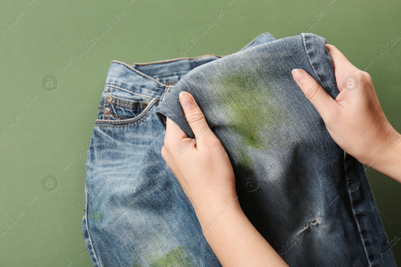 Photo of Woman holding jeans with stain on green background, closeup