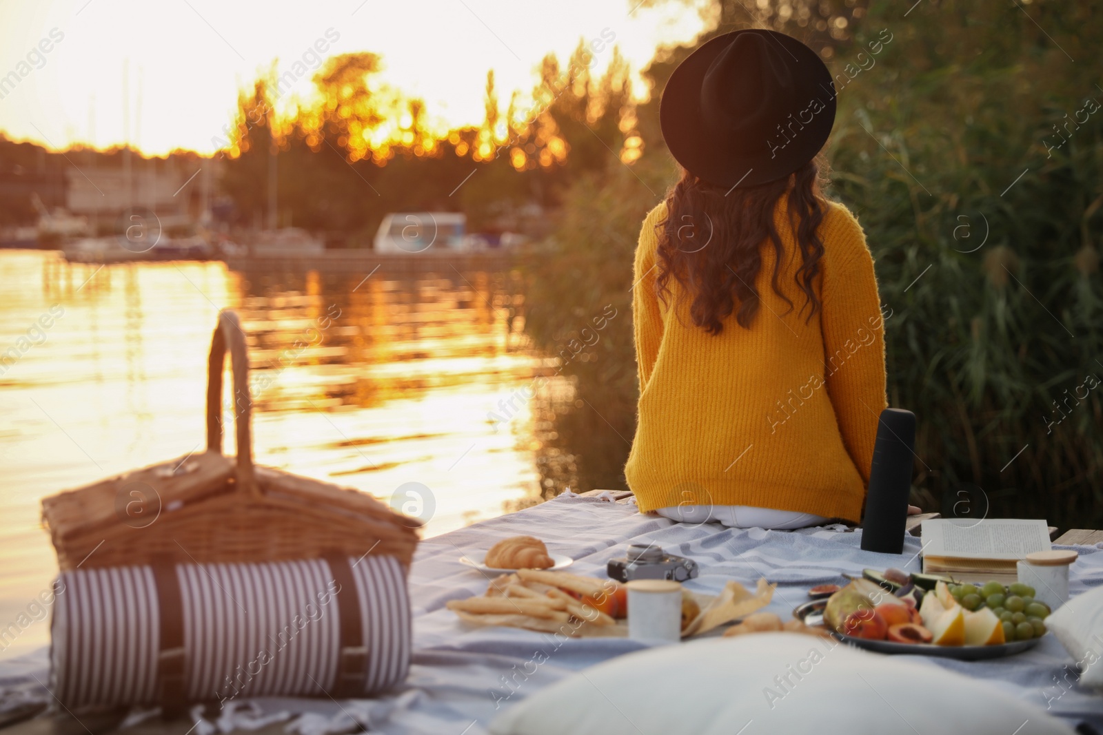 Photo of Young woman spending time on pier at picnic, back view