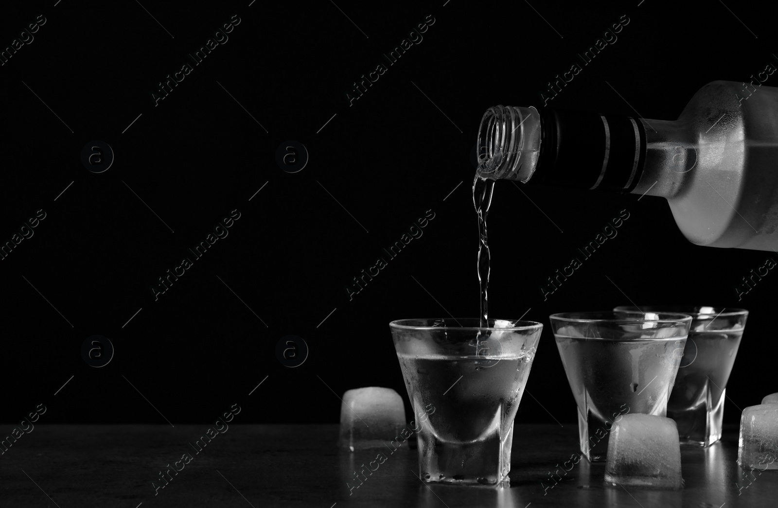 Photo of Pouring vodka from bottle in glass and ice cubes on grey table. Space for text