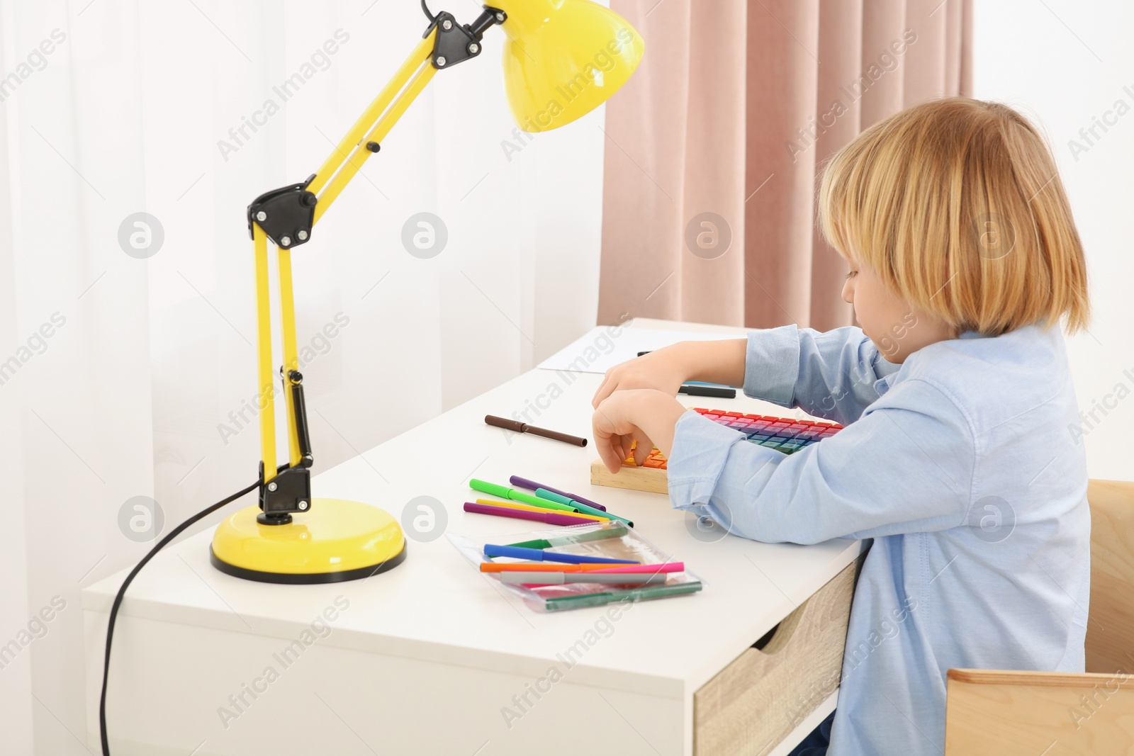 Photo of Cute little boy playing with colorful wooden cubes at desk in room. Home workplace