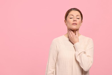 Woman suffering from sore throat on pink background. Space for text