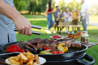 Photo of Man cooking meat and vegetables on barbecue grill in park, closeup