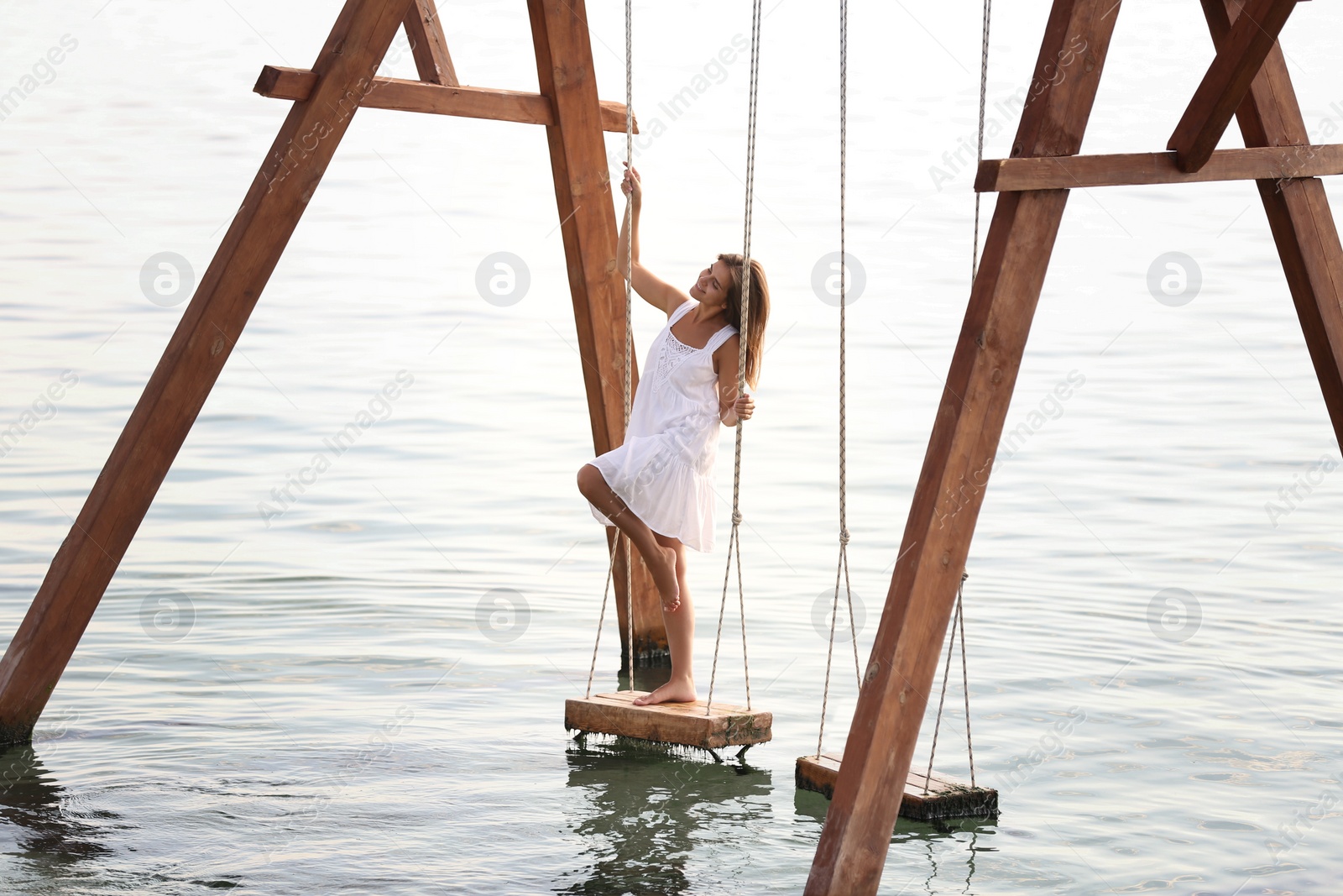 Photo of Young woman enjoying sunrise on swing over water