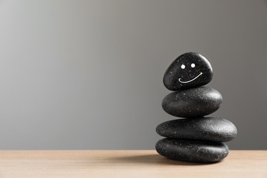 Stack of stones with drawn happy face on table against light grey background, space for text. Zen concept