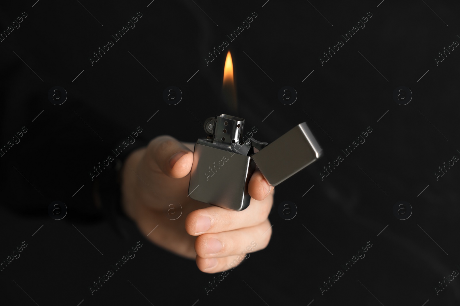 Photo of Man holding lighter with burning flame on dark background, closeup