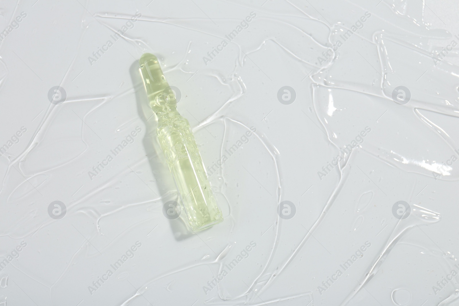 Photo of Skincare ampoule on white surface covered with gel, top view. Space for text