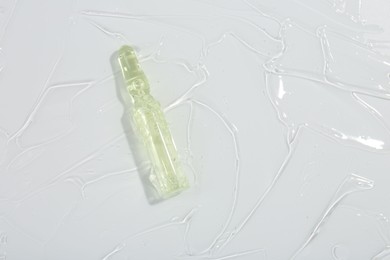 Photo of Skincare ampoule on white surface covered with gel, top view. Space for text