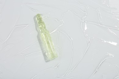 Skincare ampoule on white surface covered with gel, top view. Space for text